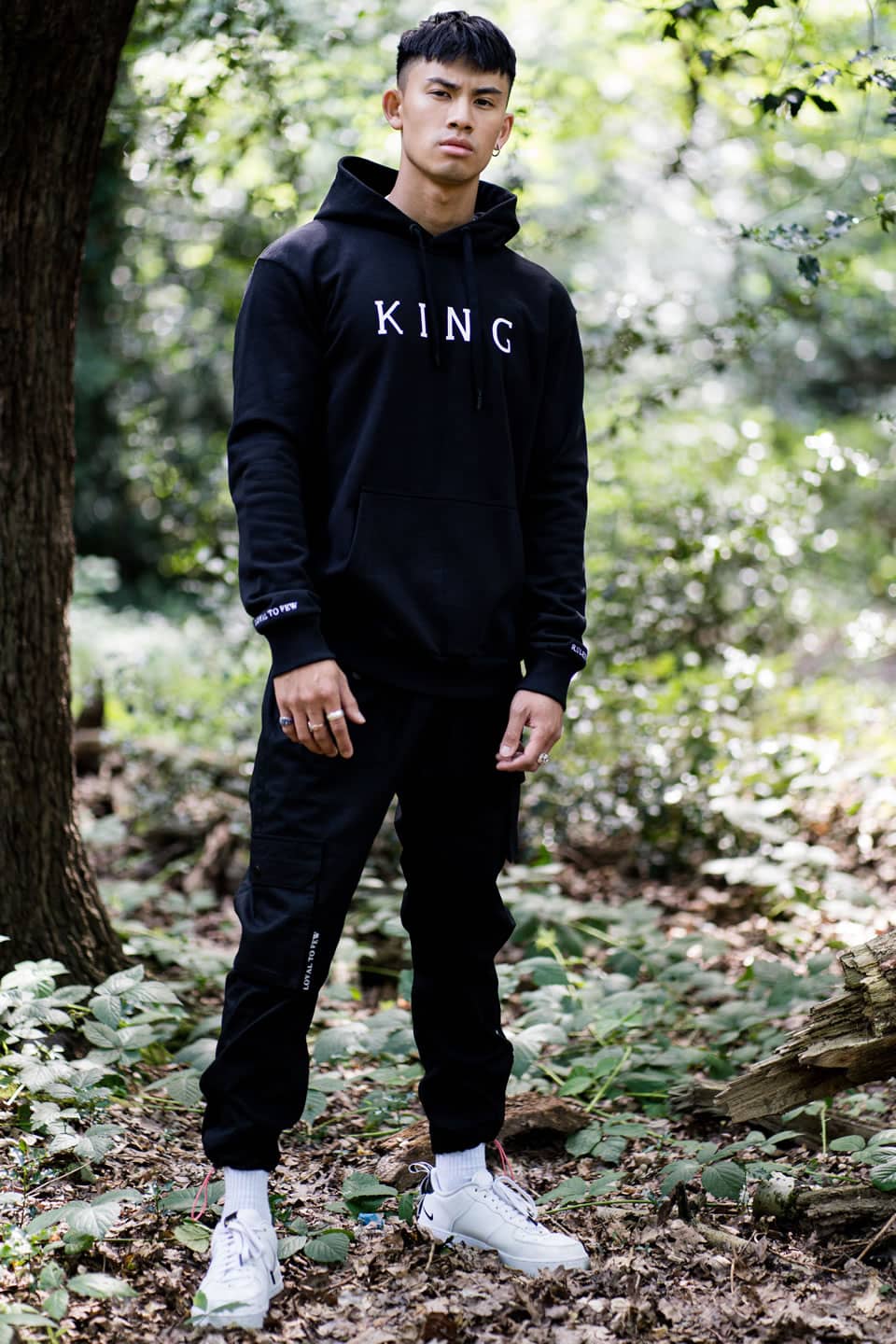 Model wears King Apparel Stepney hoodie and Earlham Techwear cargo pants in black