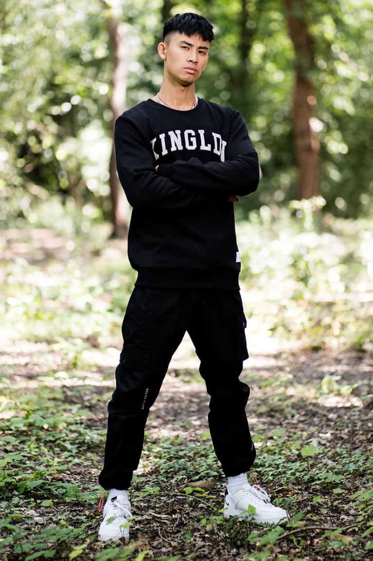 Model wears King Apparel Blackwall Varsity sweatshirt in black and Earlham Techwear cargo pants in black