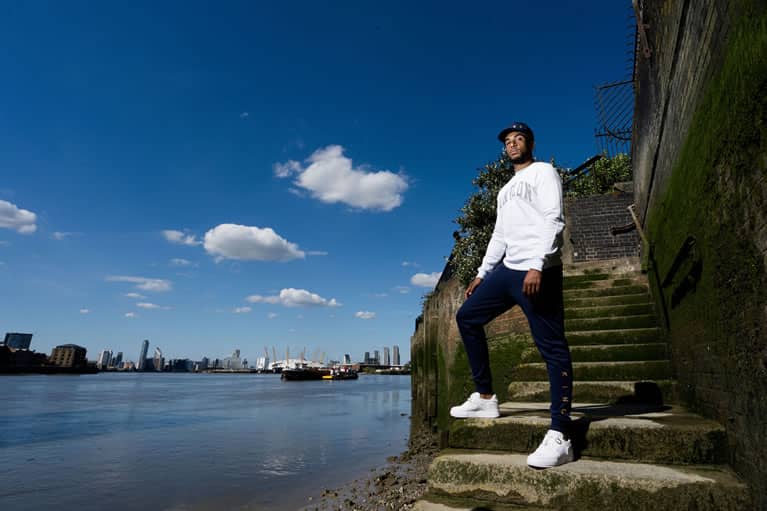 Myers wears King Apparel Blackwall Varsity sweatshirt in white and Tennyson Gold tracksuit bottoms in ink blue