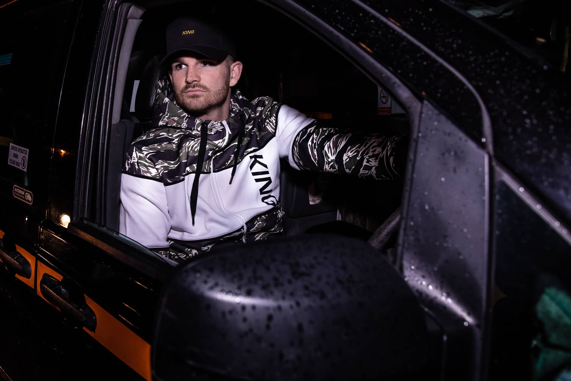 Cabbie wears King Apparel Defy curved peak cap in black and Manor tracksuit hoodie in tiger camo
