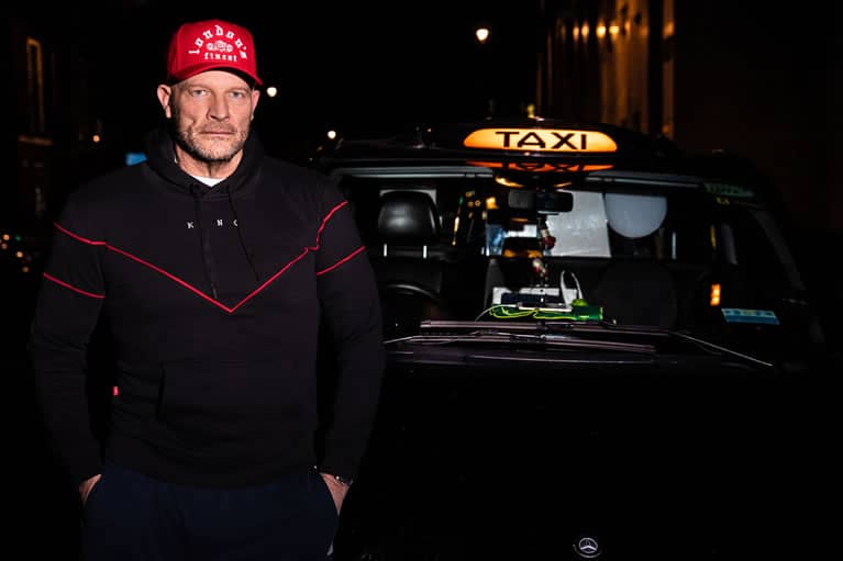 Cabbie wears King Apparel Whitechapel curved peak cap in crimson red and Tennyson tracksuit hoodie in black