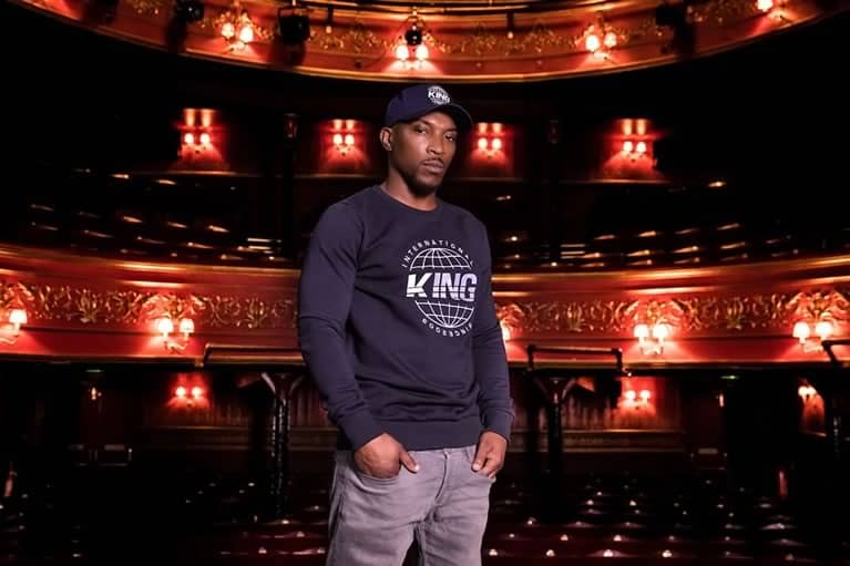 Ashley Walters wearing a KING cap and sweatshirt in a theatre